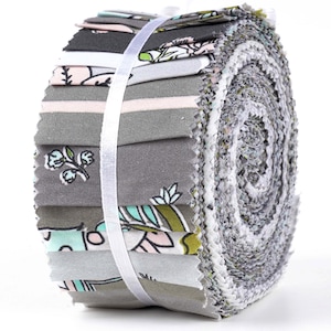 May include: A roll of fabric featuring a variety of prints in shades of gray, pink, green, and blue. The fabric is rolled up and tied with a white ribbon.
