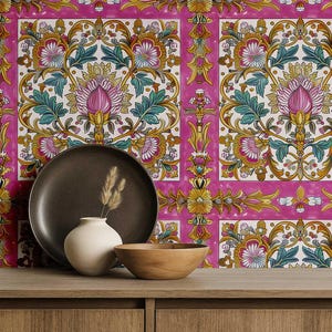 May include: A still life arrangement featuring a dark brown plate, a small white vase with dried grass, and a wooden bowl on a wooden surface. The background is a vibrant pink floral pattern with intricate designs in gold, teal, and white.