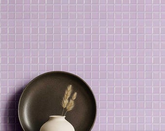 May include: A still life arrangement featuring a dark brown plate, a small white vase with dried wheat, and a wooden bowl. The background is a wall of square, lavender tiles.