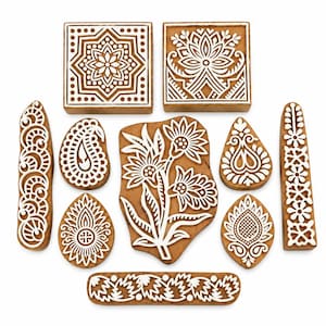 May include: A collection of ten wooden printing blocks featuring intricate white carved patterns on a natural brown wood surface. The set includes square, rectangular, teardrop, and irregular shapes with floral, geometric, and paisley motifs.