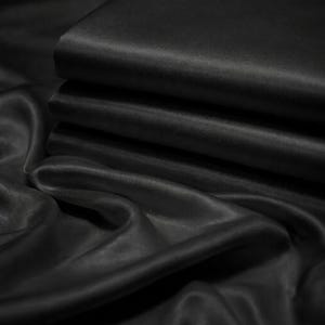 以下が含まれることがあります： 滑らかでサテンのような光沢を持つ、折り畳まれた黒い生地の山。素材は光を捉える繊細な光沢があり、ドレープ状に流れるテキスタイルの表面全体に柔らかなハイライトと深い影を作り出しています。