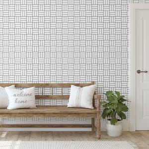 May include: A wooden bench with two decorative pillows and a houseplant in a white pot. The pillows are white with striped and script designs. The wall behind the bench has a black and white geometric pattern. A white door is on the right.