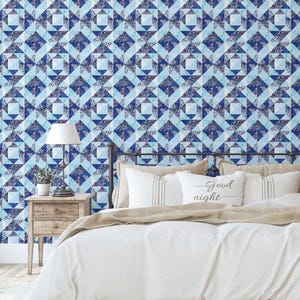 Op de afbeelding: Een slaapkamer met een bed met wit beddengoed en kussens. Het hoofdbord staat tegen een muur bedekt met blauw en wit geometrisch behang. Een nachtkastje met een lamp en een kleine plant is zichtbaar.