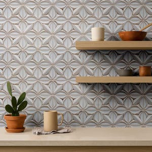 May include: A decorative wall featuring a repeating floral pattern in shades of white and beige. Two wooden shelves hold a variety of ceramic bowls and a mug. A small potted cactus and a beige mug sit on the counter.