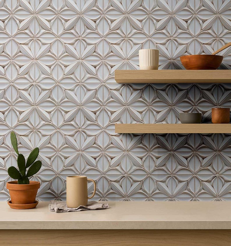 May include: A decorative wall featuring a repeating floral pattern in shades of white and beige. Two wooden shelves hold a variety of ceramic bowls and a mug. A small potted cactus and a beige mug sit on the counter.