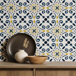 May include: A decorative arrangement featuring a dark brown plate, a small white vase with dried grass, and a wooden bowl on a wooden surface. The background showcases a patterned tile design with blue, yellow, and white floral motifs.