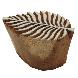 May include: A wooden block printing stamp carved in the shape of a leaf with white lines. The stamp is brown and has a rough texture.