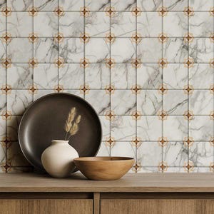 May include: A decorative arrangement featuring a dark brown plate, a small white vase with dried grass, and a wooden bowl on a wooden surface. The background is a tiled wall with a marble pattern and floral accents.