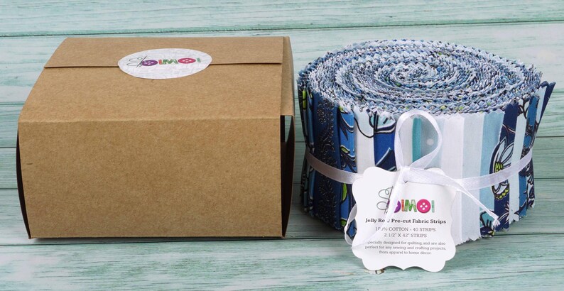 May include: A brown cardboard box with a white label that says "JIMOI" and a roll of pre-cut fabric strips in blue, white, and green patterns. The fabric strips are 2.5 inches wide and 40 strips are included in the roll. The label also says "Jelly Roll - Pre-cut Fabric Strips".