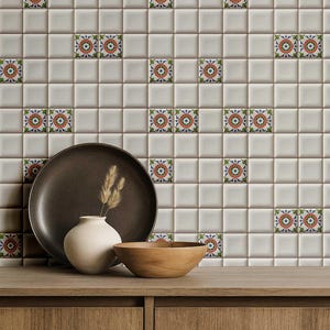 May include: A decorative wall of square, off-white tiles with patterned accent tiles. A dark brown plate, a white vase with dried grass, and a wooden bowl sit on a wooden surface in front of the tiles.