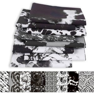 Peut inclure: Une pile de tissus pliés avec divers motifs noirs et blancs. Les motifs comprennent des dessins abstraits, des motifs tie-dye et des imprimés animaliers. Les tissus sont soigneusement disposés, mettant en valeur les textures et les styles variés.