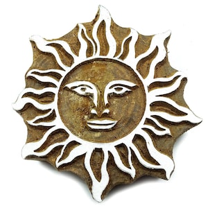 May include: A wooden block printing stamp shaped like a sun with a smiling face. The sun has white rays and a brown face with white eyes and a mouth.