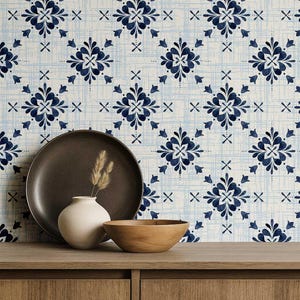 May include: A decorative arrangement featuring a dark brown plate, a small white vase with dried stems, and a wooden bowl on a wooden surface. The background showcases a patterned wallpaper with blue floral designs.