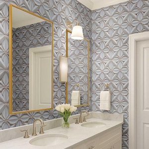 May include: A modern bathroom with a white vanity, two sinks, and a marble countertop. The walls are adorned with a textured, light blue and gray floral tile design. Gold-framed mirrors and sconces add a touch of elegance. A vase of white tulips sits on the counter.