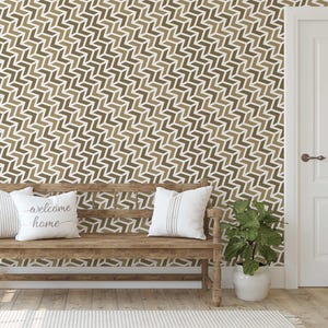 May include: A wooden bench with white pillows and a decorative wall with a repeating chevron pattern in shades of brown and white. A potted plant sits to the right of the bench, and a white door is visible in the background.