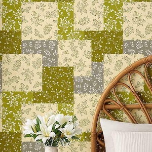 以下が含まれることがあります： オリーブグリーン、クリーム、グレーの正方形が特徴のパッチワーク模様の壁紙。各正方形は、繊細な白い花の小枝のデザインで装飾されています。花瓶に入った白いユリのブーケが前景にあります。