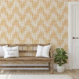 May include: A wooden bench with white pillows and a potted plant sits in front of a wall with a yellow and white grid pattern. One pillow has the words "welcome home" on it. A white door is on the right.