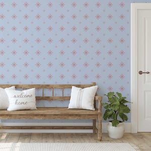 May include: A light blue wall with a repeating pattern of pink starbursts and circles. A wooden bench with white pillows sits in front of the wall. One pillow says "welcome home". A potted plant and a white door are also visible.