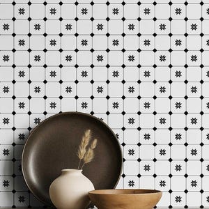 Peut inclure: Une composition décorative avec une assiette marron foncé, un petit vase beige contenant du blé séché et un bol en bois. Le fond est un motif de carreaux blancs avec des motifs d'éclats noirs.