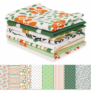 May include: A stack of folded kitchen towels with various patterns. The top towel features orange floral designs on a white background. Other towels display green, orange, and yellow stripes, polka dots, and floral patterns. The towels are stacked on a white background.