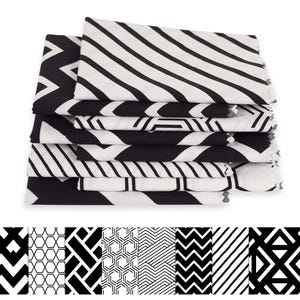 May include: A pile of folded fabric swatches featuring black and white geometric designs. Patterns include stripes, zigzags, and angular shapes. The swatches are stacked, displaying a range of fabric styles and patterns.