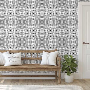 May include: A room featuring a wooden bench with white pillows, one with "welcome home" text. The wall has a black and white geometric pattern. A potted plant sits beside the bench, and a white door is visible.