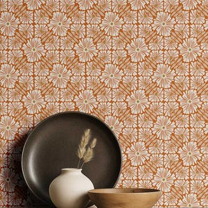 May include: A still life arrangement featuring a dark brown plate, a small white vase with dried grass, and a wooden bowl. The background is a repeating floral pattern in white, orange, and light green.