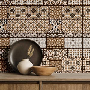 Op de afbeelding: Een decoratieve opstelling met een donkerbruine keramische schotel, een kleine witte vaas met gedroogd gras en een houten kom. De achtergrond toont een betegelde muur met bruine, beige en witte geometrische patronen. De objecten staan op een houten oppervlak.