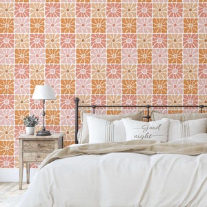 May include: A bedroom scene featuring a floral wallpaper in shades of pink, orange, and beige. The wallpaper's repeating pattern is a grid of stylized flowers. The bed has white bedding and pillows, with a pillow that says "Good night".
