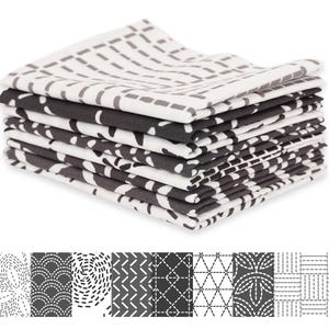 May include: A stack of six folded cloth napkins with various black and white geometric patterns. The patterns include dashes, curved lines, and zigzags. The napkins are neatly arranged, showcasing the different designs.