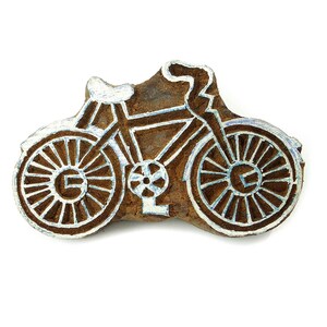 May include: A wooden block carving of a bicycle with white paint outlining the design. The bicycle has a detailed design with spokes on the wheels.