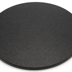 May include: A solid black, round object with a textured surface. The object is a flat disc, likely a coaster or a similar item. The edges are smooth and the overall appearance is minimalist and modern.