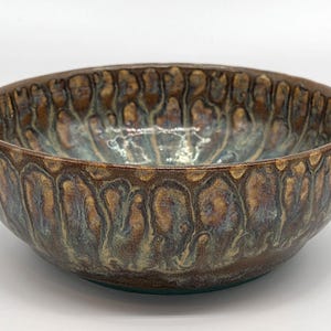 May include: A handmade ceramic bowl with a textured, organic design. The bowl features a rich color palette of brown, gold, and teal, with a glossy finish. The bowl's exterior has a repeating pattern, and it measures approximately 8 inches in diameter.