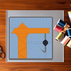 May include: A quilting project featuring an orange crane design on a light blue background. The image includes scissors, spools of thread in various colors, and a small quilt piece, all arranged on a wooden surface.