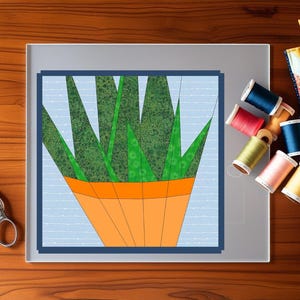 Puede incluir: Un bloque de patchwork colorido con un diseño de planta verde y naranja, sobre un fondo azul claro. La imagen incluye tijeras, carretes de hilo de varios colores y un pequeño edredón de patchwork, lo que sugiere un proyecto de costura.