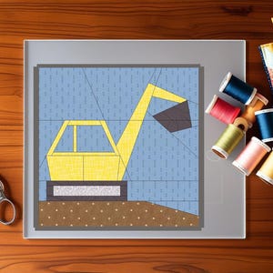 May include: A yellow excavator quilt block design on a light blue background, with a brown base. The image includes spools of thread in various colors, scissors, and a small quilt. The scene is set on a wooden surface.