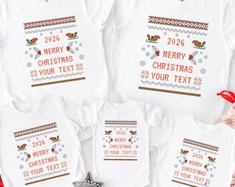May include: A collection of white Christmas-themed t-shirts and a babygrow. Each garment displays a festive design with snowflakes, sleds, and the text "2026 Merry Christmas Your Text" in red and brown. Cookies and a star are also visible.