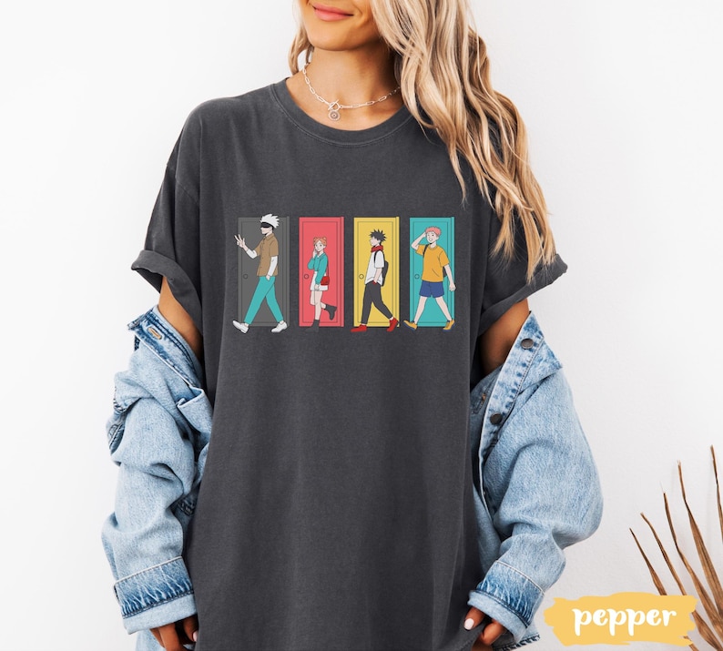 May include: Dark gray t-shirt featuring a colorful graphic of four anime characters walking through doors. The characters are in different outfits and the doors are red, yellow, and blue. The word "pepper" is in a yellow rectangle in the bottom right corner.