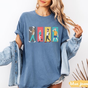 May include: Blue jean-colored t-shirt featuring a graphic of four anime characters walking through colorful doors. The characters are in different outfits and poses. The text "blue jean" is at the bottom right.