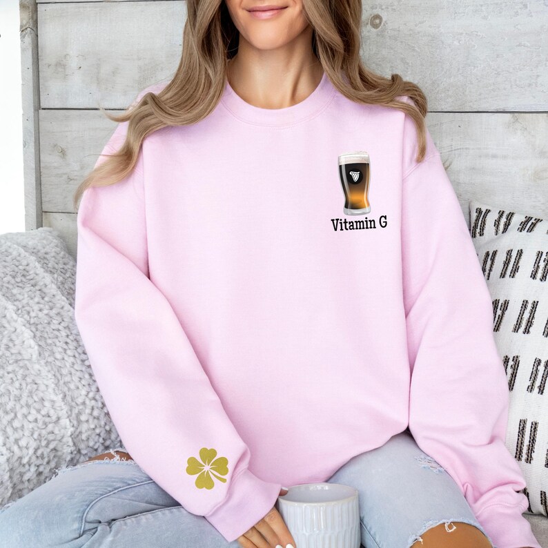 Może przedstawiać: Jasnor&oacute;żowa bluza z nadrukiem kufla piwa i napisem "Vitamin G". Złota czterolistna koniczyna znajduje się na lewym rękawie. Bluza jest w stylu casual.