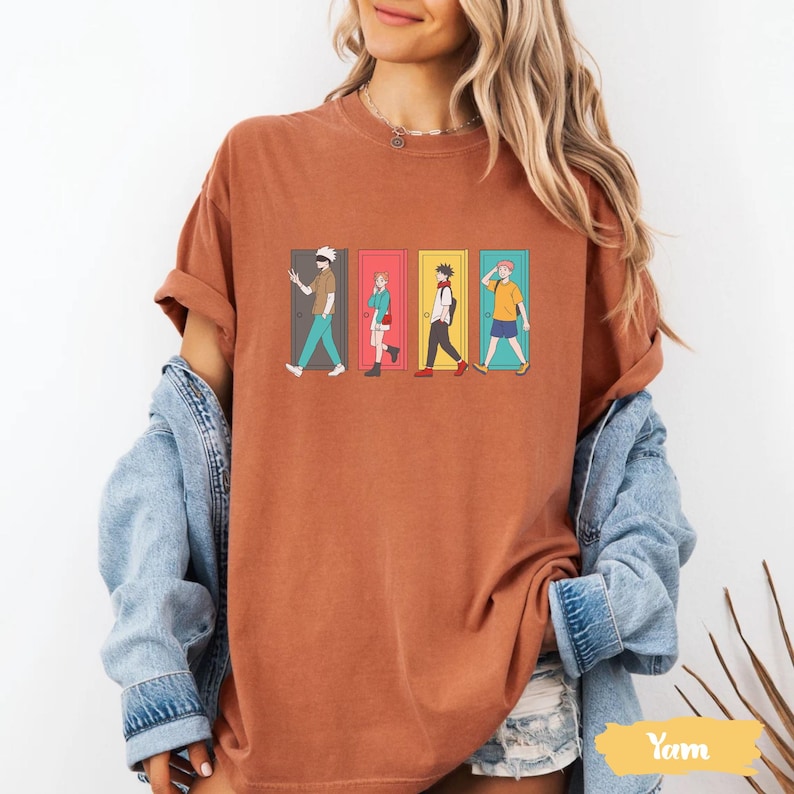 May include: Rust-colored t-shirt featuring a graphic of four anime characters walking through colorful doors. The design includes characters in various outfits, with doors in green, pink, yellow, and blue. The shirt is a casual wear item.