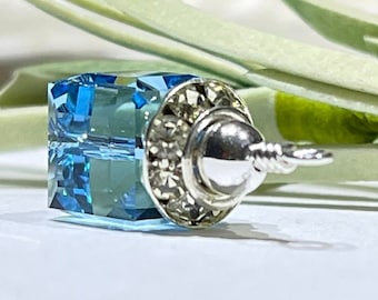 May include: A square blue crystal charm with a silver cap and a silver loop. The crystal is faceted and has a light blue colour.
