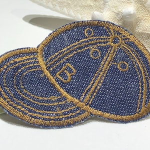 Puede incluir: Un parche de tela vaquera azul con un diseño bordado en oro de una gorra de béisbol. El parche es perfecto para agregar un toque único a la ropa, bolsos u otros accesorios.