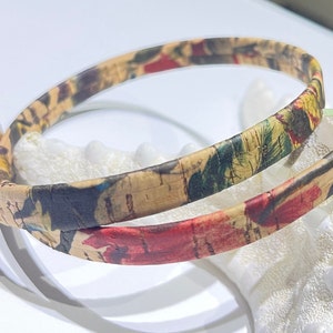 Puede incluir: Pulsera decorativa de corcho con un estampado floral en rojo, verde, amarillo y azul. La pulsera tiene un diseño en espiral, mostrando la textura natural del corcho. Diámetro aproximado de 18 cm.