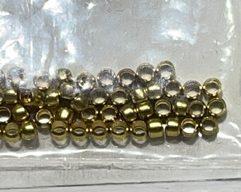 May include: A close-up of a plastic bag filled with gold-coloured metal beads. The beads are small and round, with a hole in the centre.