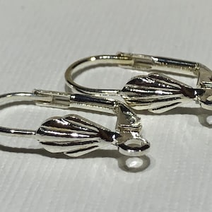 Puede incluir: Dos ganchos para pendientes de color plateado con un diseño en forma de concha. Los ganchos son de metal y tienen un cierre de resorte.