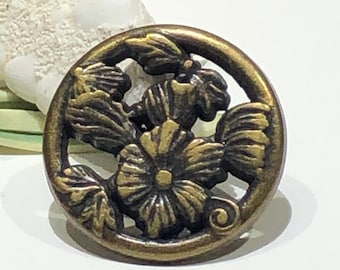 May include: A round, antique gold-toned metal button with a floral design. The button features a raised, detailed design of three flowers with leaves and a swirl.