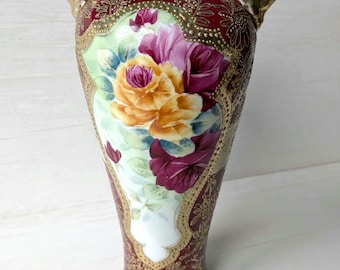 Peut inclure: Un vase orné avec un design bordeaux et or. Le vase présente une peinture florale avec des roses jaunes et violettes. Il a deux poignées dorées et un motif détaillé et texturé.