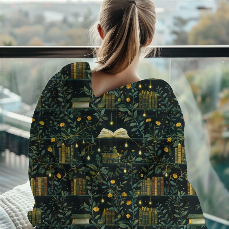 May include: A dark blanket featuring a pattern of bookshelves, books, yellow flowers, and fairy lights. The blanket is draped over a person's shoulders, with the person facing away from the camera. The background shows a blurred window view.