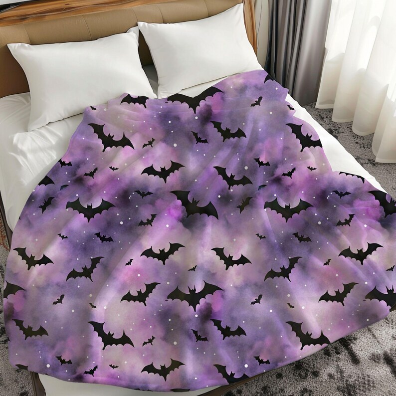May include: A purple and lavender blanket with a pattern of black bats and white specks. The blanket is draped over a bed with white pillows. The design has a Halloween theme.